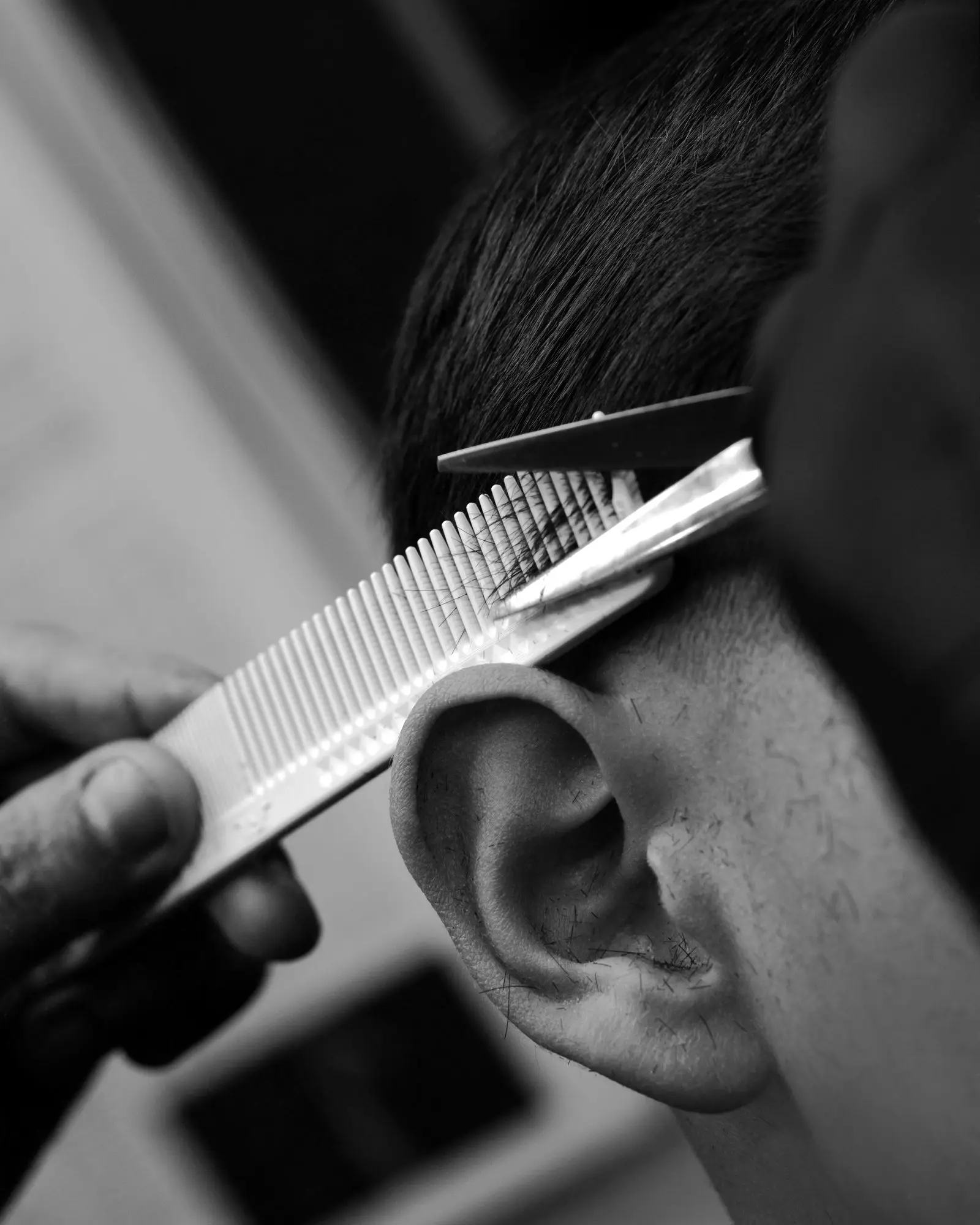 Detalle en blanco y negro: Dazs sostiene un peine y una tijera junto a la oreja de un cliente.