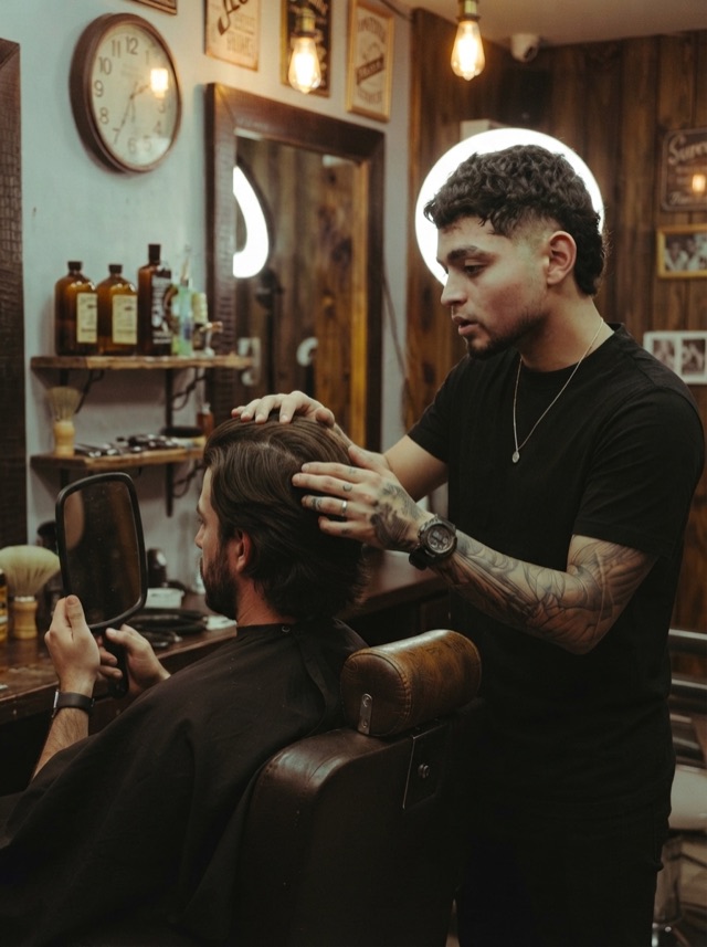 Barbero toma el pelo del cliente mientras este se mira en un espejo de mano