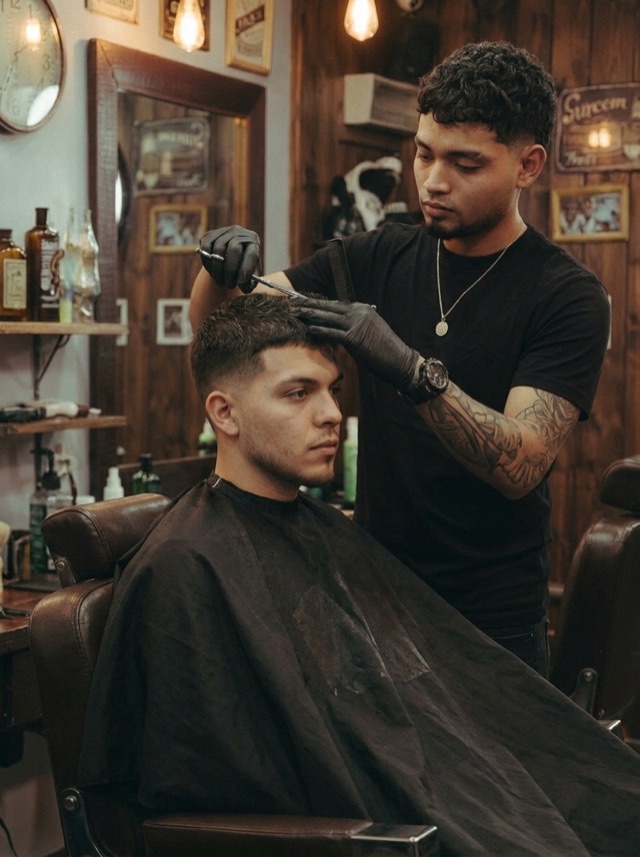 Barbero con guantes corta el pelo de un cliente cubierto con una capa